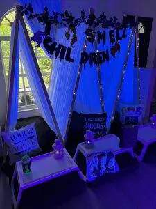 A dimly lit indoor setup featuring a white tent with hanging lights, cushions, and themed decorations. A banner reads "Chill Smell Dren." Pillows display Halloween-themed designs and text, creating the perfect atmosphere for a kids slumber party rental.