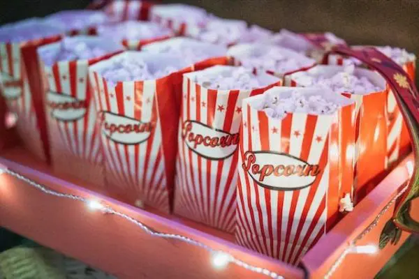 Several red-and-white striped popcorn bags filled with popcorn are displayed on a tray adorned with string lights, perfect for a slumber party.