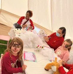 Children and adults sitting at a table making stuffed animals, surrounded by cotton stuffing, craft supplies, and plush toys—a delightful kids party rental experience.