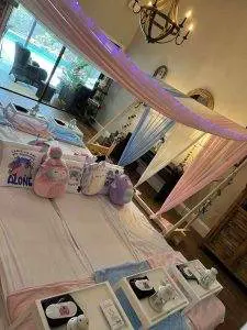 Interior of a room set up for a kids sleepover with draped pastel fabrics, led lights, and personalized sleeping setups, including cushions and trays on mattresses.