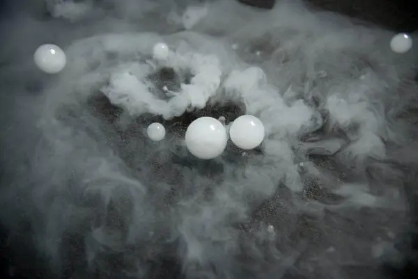 White spheres and swirling mist from a Frogger F4 Bubble Fogger Rental on a textured surface, creating an ethereal atmosphere.