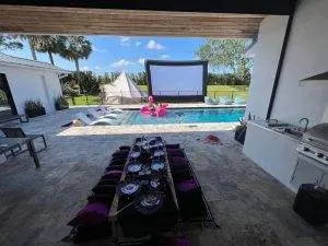 Luxurious outdoor patio with a dining area, overlooking a swimming pool with an inflatable flamingo and a large movie screen, perfect for hosting parties in Winter Haven.