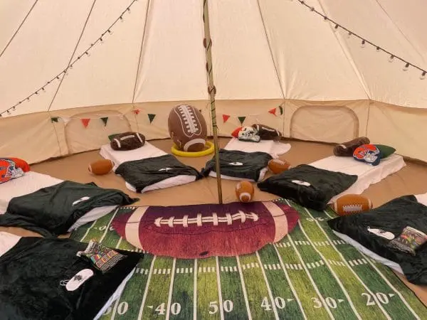 Inside a tent decorated with football-themed bedding and accessories for event planning, including a large rug resembling a football field and helmets.