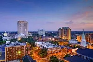 Aerial view of a city at dusk showing illuminated buildings, a high-rise tower, and tree-lined streets under a twilight sky in the areas we serve.