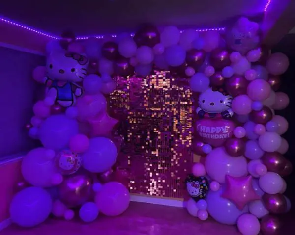 A hello kitty-themed birthday decoration with pink and purple balloons and a shimmering sequin wall, perfect for those seeking creative party themes.