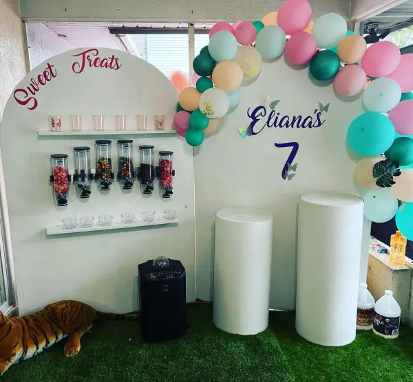 A candy bar setup at a sleepover birthday party with a sign reading "sweet treats" and "liana's 7," decorated with balloons and jars of candy. A toy tiger is on the