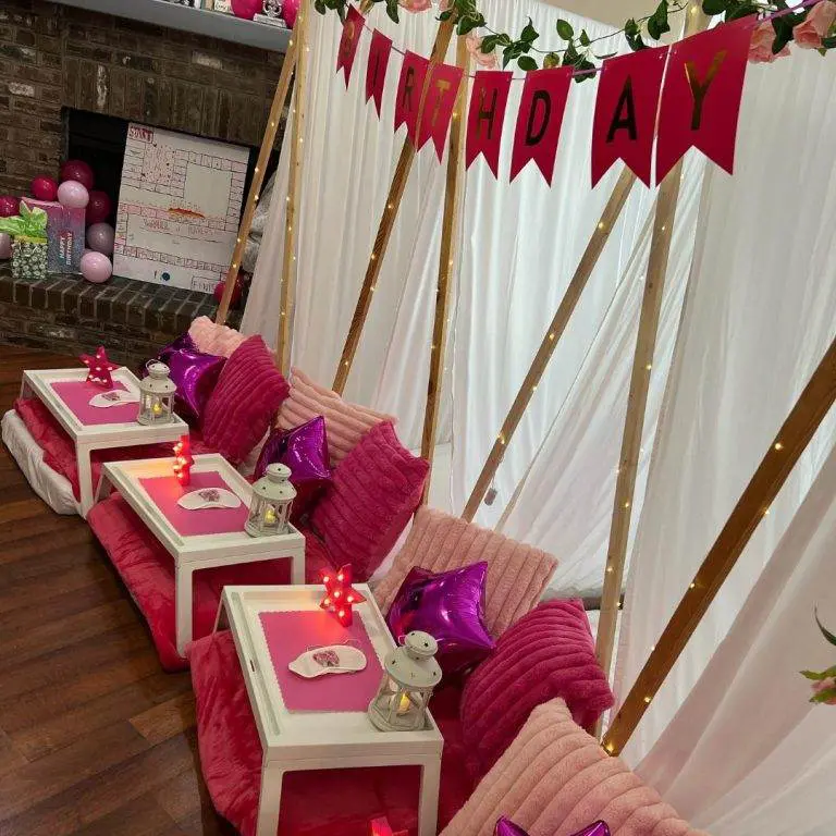 Indoor birthday party setup with pink-themed decor, including velvet seats, white tables, birthday banners, balloons, and unique party themes.