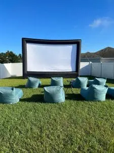 Outdoor movie screening setup with an inflatable screen and multiple bean bag chairs on a grassy lawn, under a clear sky, perfect for the ultimate adult party.