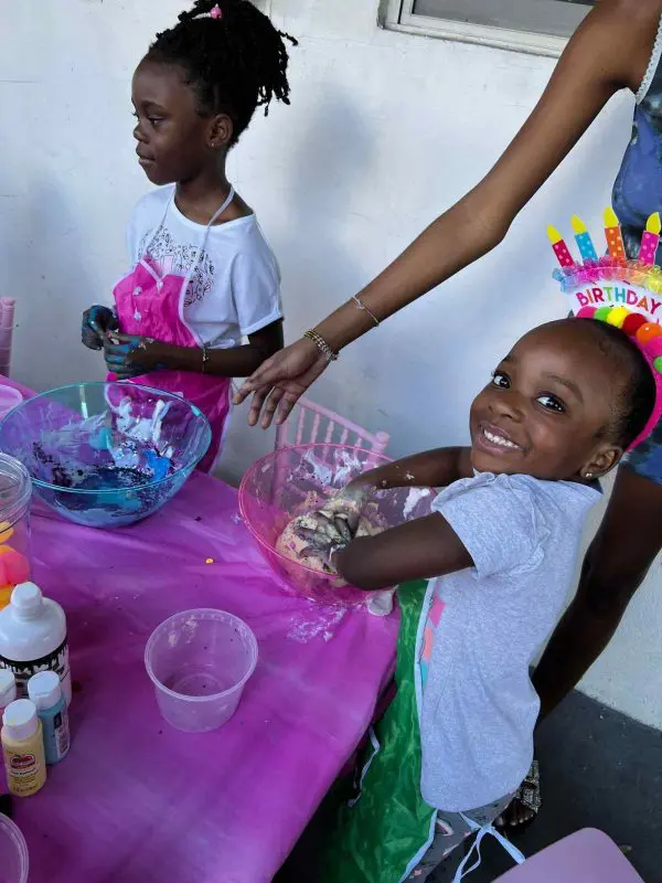 Two young girls engaging in a craft activity at a sleepover, smiling while mixing colorful paint in bowls.