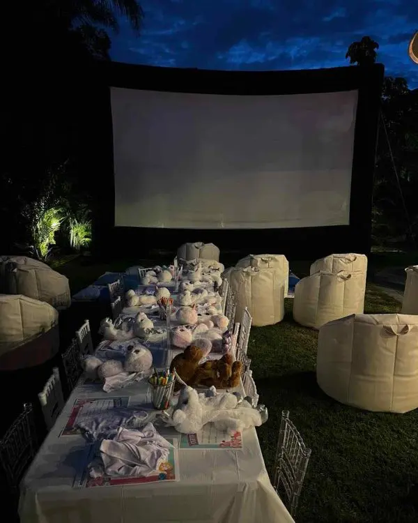 Outdoor movie night setup with bean bags and stuffed animals facing a large screen in a garden at dusk, perfect for the 2024 Ultimate Sleepover.