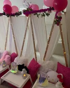 Indoor teepee tents adorned with pink balloons, string lights, and cozy cushions for an Ultimate Slumber Party setup.