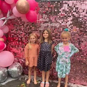 Three young girls standing in front of a pink decoration with balloons and a sign reading "hello gorgeous" at the 2024 Ultimate Sleepover.