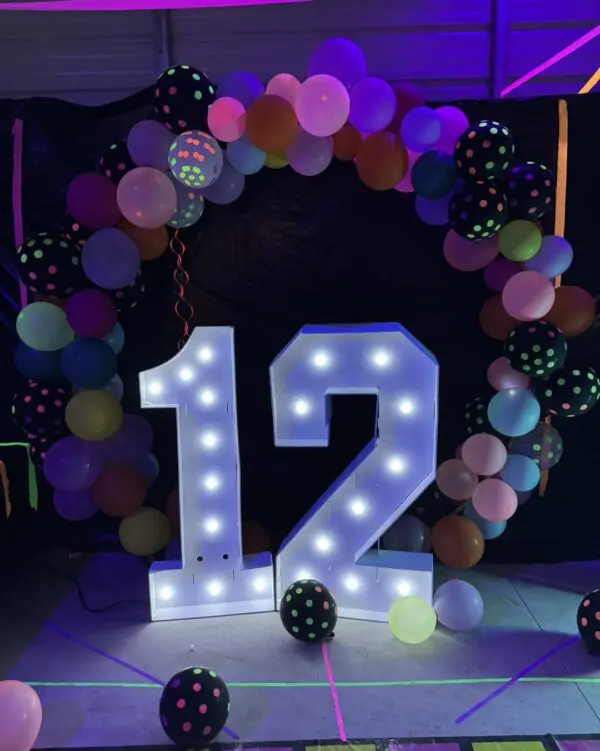 In the captivating setting of a Movie Night Extravaganza, a radiant illuminated number 12 takes center stage, surrounded by a stunning arch of colorful balloons adorned with playful polka dot patterns. This vibrant and festive display pops against the deep, dark background, perfectly capturing the essence of celebration and excitement. Ideal for events or parties seeking that cinematic magic and Instagram-worthy moments!