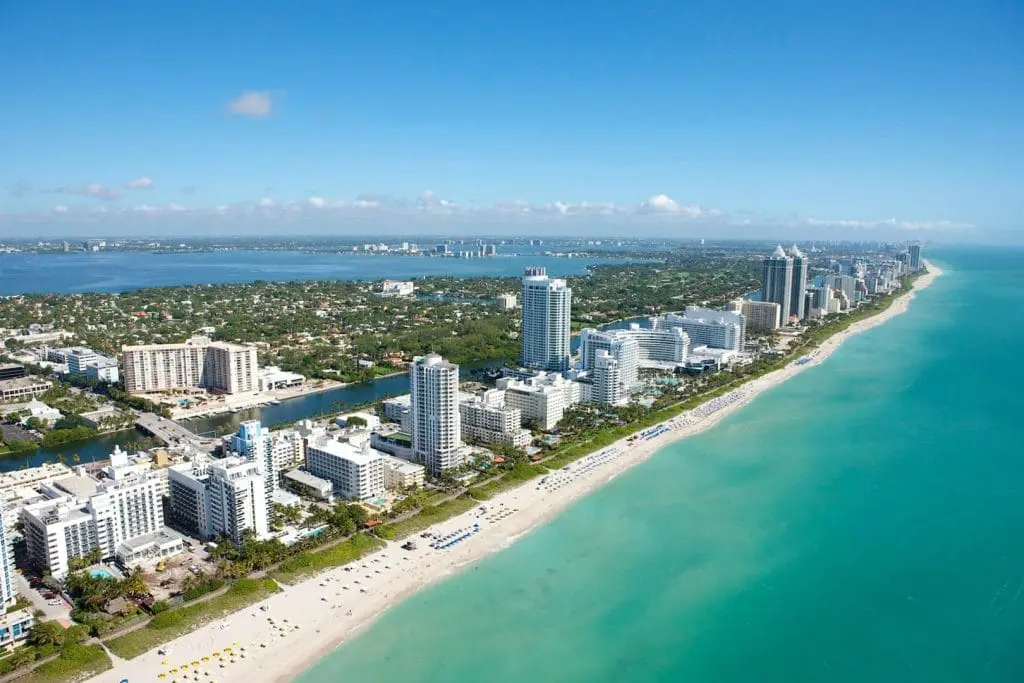 Aerial view of a coastal city with towering skyscrapers along a turquoise beach, extending towards a clear horizon. Miami party rentals by the beach