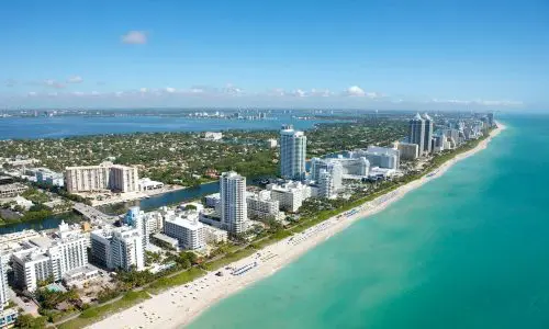 Aerial view of a coastal city with towering skyscrapers along a turquoise beach, extending towards a clear horizon. Miami party rentals by the beach