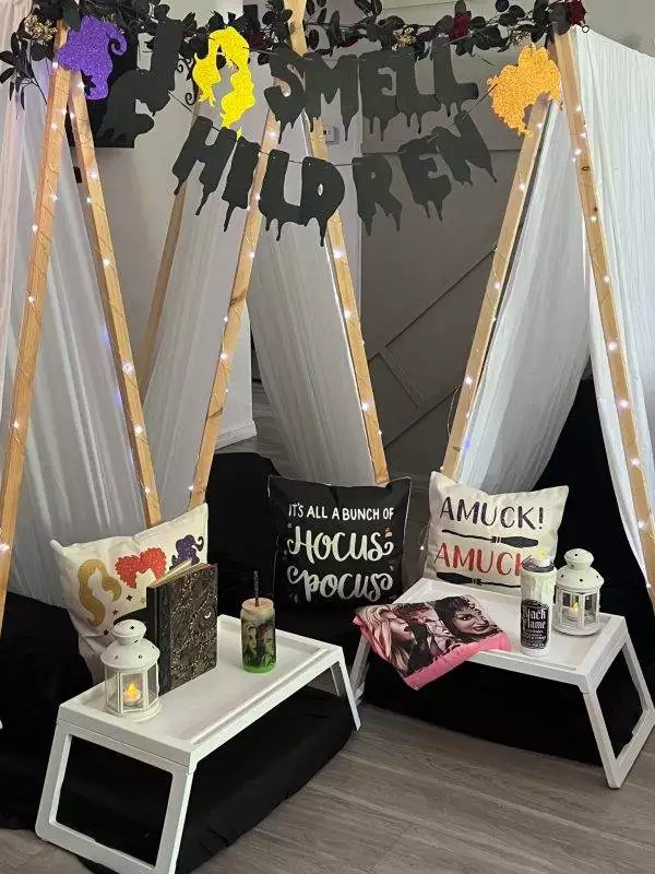 Two indoor tents decorated with Halloween-themed items, including an "I Smell Children" banner, pillows with spooky designs, lanterns, and a themed book resting on small white tables. Perfect for any kids party rental, this setup brings festive fun to your next gathering.