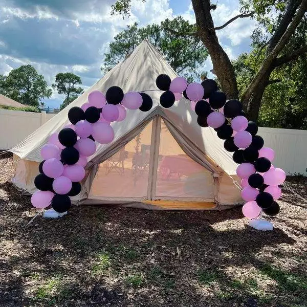 A canvas bell tent decorated with a balloon arch in black and pink, set up outdoors under a clear sky, accessible through an appointment booking.