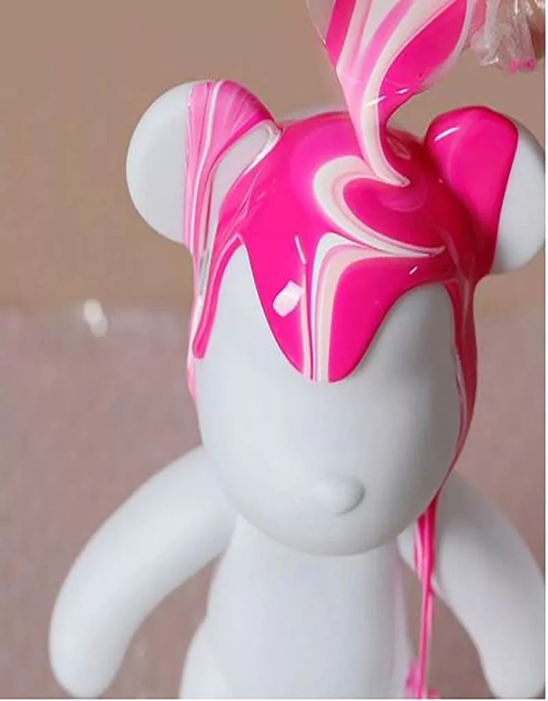 A white bear-shaped figurine is being covered with swirled pink and white liquid, likely paint or slime, as if it's the star of a playful slime party where creativity roams free and imaginations run wild.