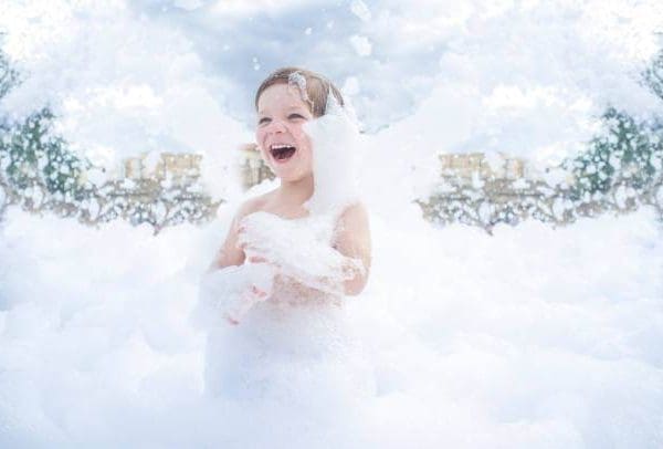 A child is joyfully playing in an outdoor area filled with foam, reminiscent of a fun slime party, surrounded by a frothy, cloud-like environment under a partly cloudy sky.