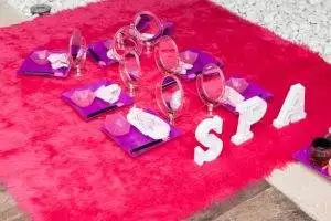 A cozy spa setup on a bright pink furry rug with small mirrors, towels, and spa tools arranged on purple trays. White letters spell out "SPA" on the right side. Perfect for a unique party rental, this teepee-inspired arrangement adds a whimsical touch to any celebration.