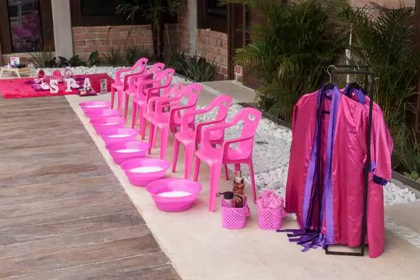 A row of pink chairs with foot basins is arranged next to a rack of colorful robes, perfect for a slumber party.