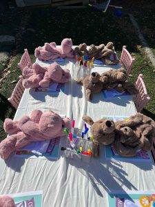 Stuffed animals sitting around small tables with party activities, outdoors on a sunny day.