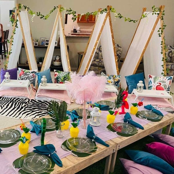 Artistic craft station setup with easels, decorations, and a table set for a creative workshop or tropical birthday party, featuring colorful accents and festive decor.