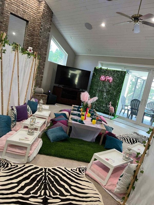 Living room decorated for a tropical slumber party with low seating, zebra print rugs, and a pink floral backdrop.