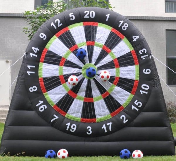 Inflatable dartboard with velcro soccer balls stuck on various numbers, located on a grass field in front of a building, perfect for birthday party add-ons.