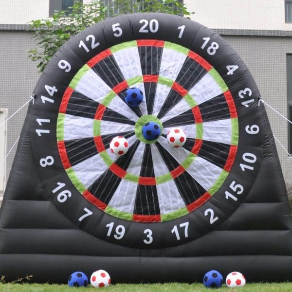 Inflatable dartboard with velcro soccer balls stuck on various numbers, located on a grass field in front of a building, perfect for birthday party add-ons.
