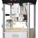 A commercial popcorn machine with a clear glass enclosure and stainless steel base, filled with freshly popped popcorn, perfect for birthday party add-ons.