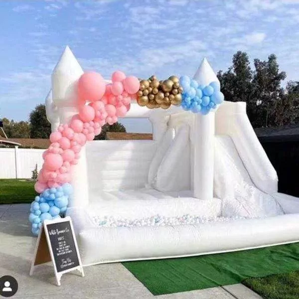 Inflatable bounce house with a slide, decorated with pink and blue balloons, set up on a lawn for a birthday event.
