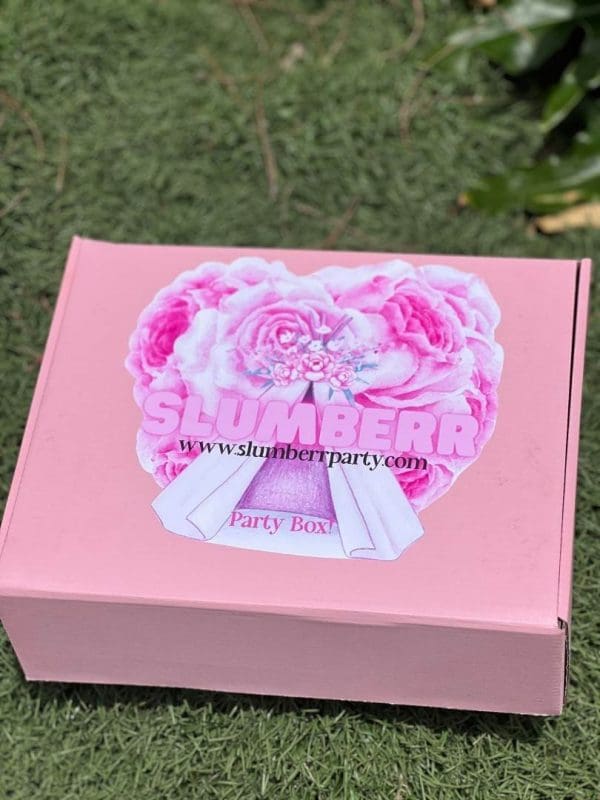 A pink Slime Party Box with a floral design and the words "slime party box" on a grassy background.