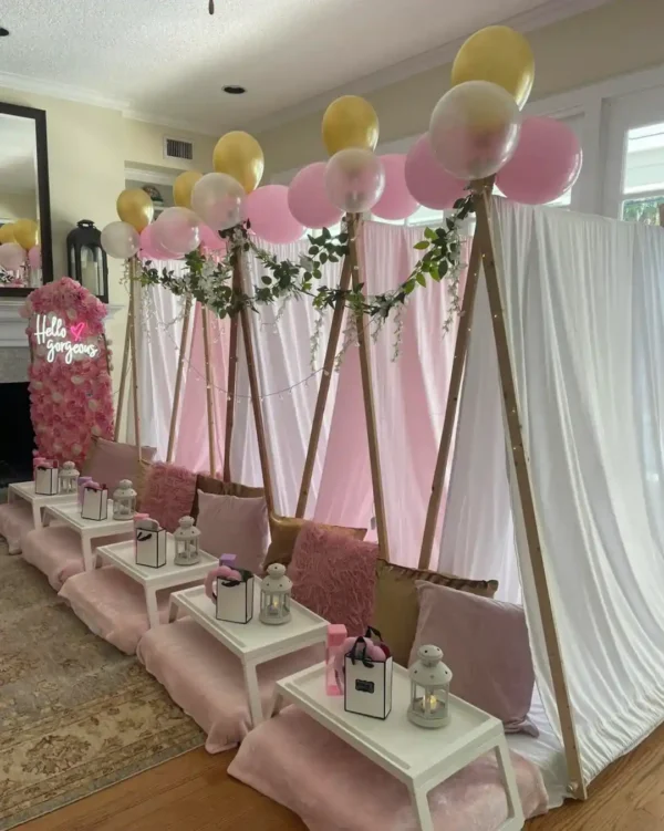 Indoor setup with small white tents draped in pink and white fabric, decorated with balloons, greenery, cushions, trays, lanterns, gift bags, and our Shimmer Backdrop Wall Rental for a magical party or sleepover.
