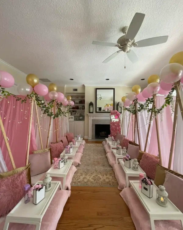 A pink and gold-themed indoor party room features two rows of teepee tents, balloons, gift boxes, cozy cushions, and a Shimmer Backdrop Wall Rental sparkling next to the fireplace.