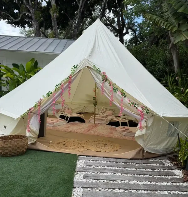 A large white canvas tent with floral garlands, rugs, low tables on a wooden deck and artificial grass—paired with our Shimmer Backdrop Wall Rental for an extra touch of elegance at your outdoor event.
