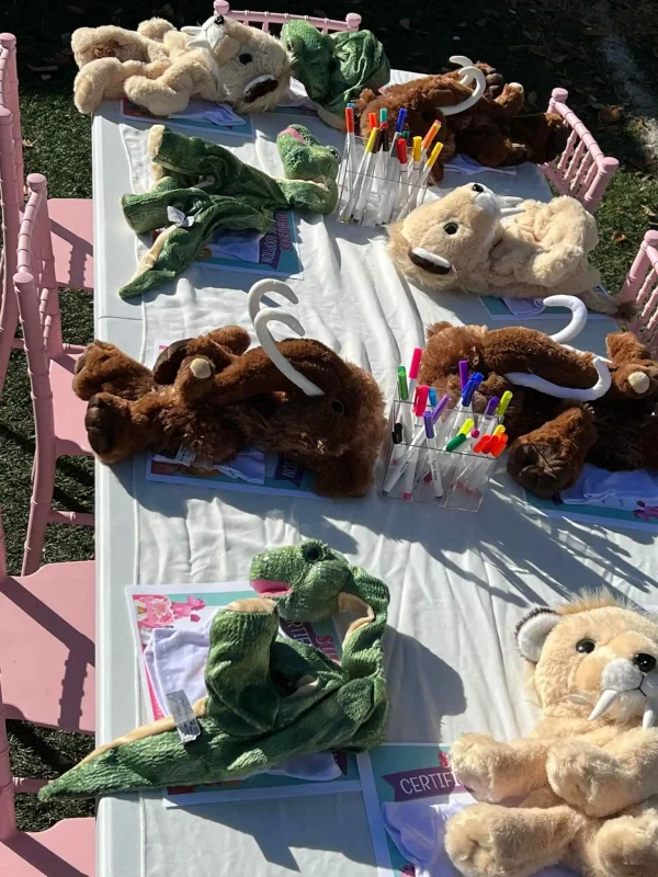 Plush animal heads on a table with colored markers and papers, set up for a Slumberr kids party activity outdoors in Central Florida.