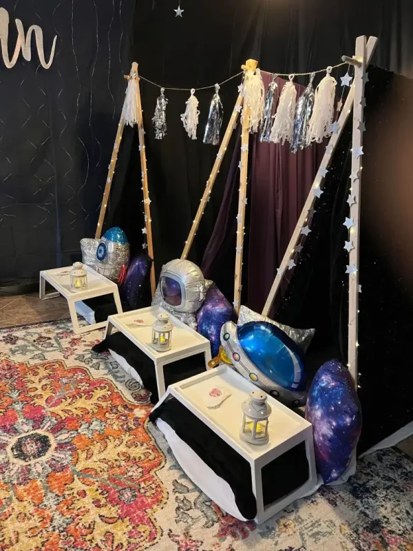 A children's play area featuring a wooden swing, colorful space-themed cushions, rugs, and decorative elements like stars and enchanting teepees.