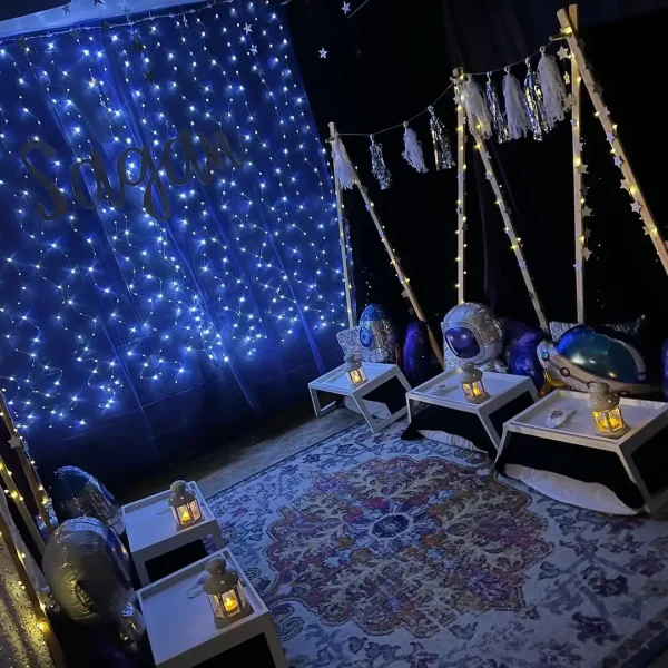 Dark-themed sensory room decorated with twinkling blue lights, hanging stars, and space-themed cushions on swings and an enchanting teepee.