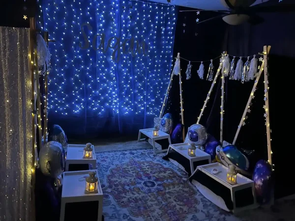 A dimly lit room decorated with a "dream" sign in blue lights, featuring four swing chairs and star motifs, creating a tranquil, enchanting teepee atmosphere.