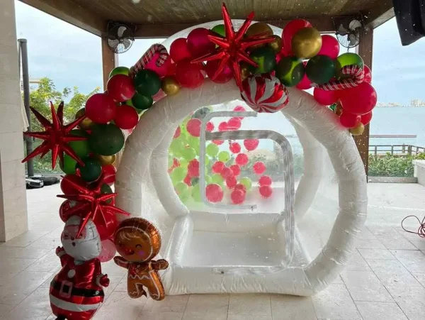 Inflatable holiday-themed photo booth with red and green balloons and decorations, set up near a water view at a wonderland event.