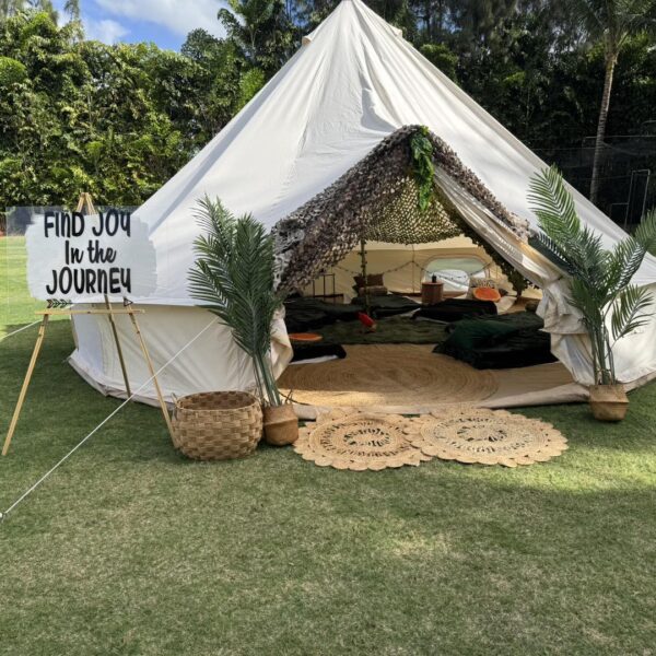 Vibrant Camping Party Tent in Green Field Setting - Step into an enchanting outdoor gathering space with our white "Camping Party Theme" tent, perfectly pitched on a lush grassy field. The tent's open entrance invites you to explore a cozy interior adorned with soft cushions and plush blankets, creating an inviting haven for relaxation and socializing. Outside, a charming sign reading "Find Joy in the Journey" greets guests, beautifully complemented by vibrant potted plants that enhance the warm and welcoming ambiance. Ideal for unforgettable outdoor celebrations or serene retreats amidst nature's embrace.