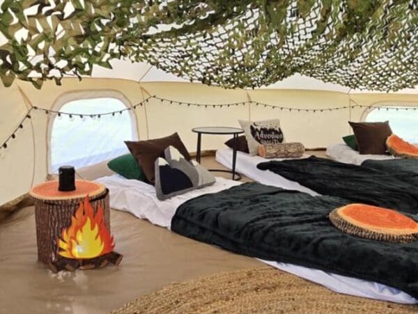 Immerse yourself in a charming camping party-themed tent, where adventurous decor and cozy comforts await. Nestled within this woodland retreat are two inviting beds draped in rustic charm, surrounded by lifelike faux logs and lush leaves that evoke the serene beauty of nature. A quaint round table sits between the beds, creating an ideal spot for sharing delightful campfire stories under the imaginary starlit sky. Escape to this enchanting indoor campsite that perfectly blends outdoor allure with indoor coziness, ensuring a unique and unforgettable experience.