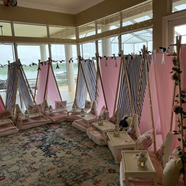 Interior of a sunroom with draped pink and striped canopies over individual pedicure stations, decorated with flowers, and an ocean view, designed to reflect a Night In Paris Theme event.