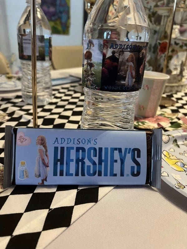 Customized Hershey’s chocolate bar labeled "Addison's" with images, placed in front of a personalized water bottle on a Wonderland Wonders checkered tablecloth.