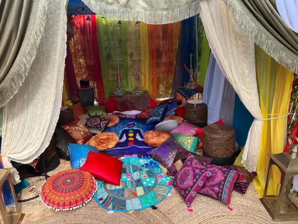 A vibrant, Alice in Wonderland party-themed lounge area with colorful curtains, assorted cushions, and low seating under a tent.