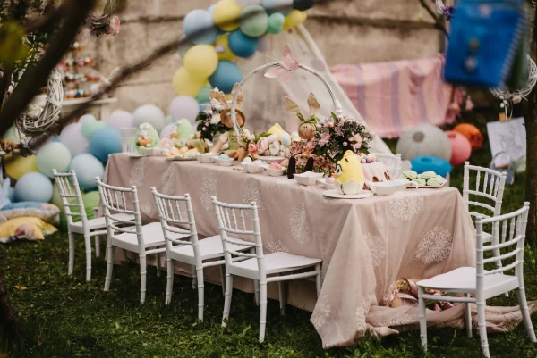 Elegant outdoor children's party setup with a Kids Table and Chair Rental adorned with pastel decorations, floral centerpieces, and colorful balloons in the background.