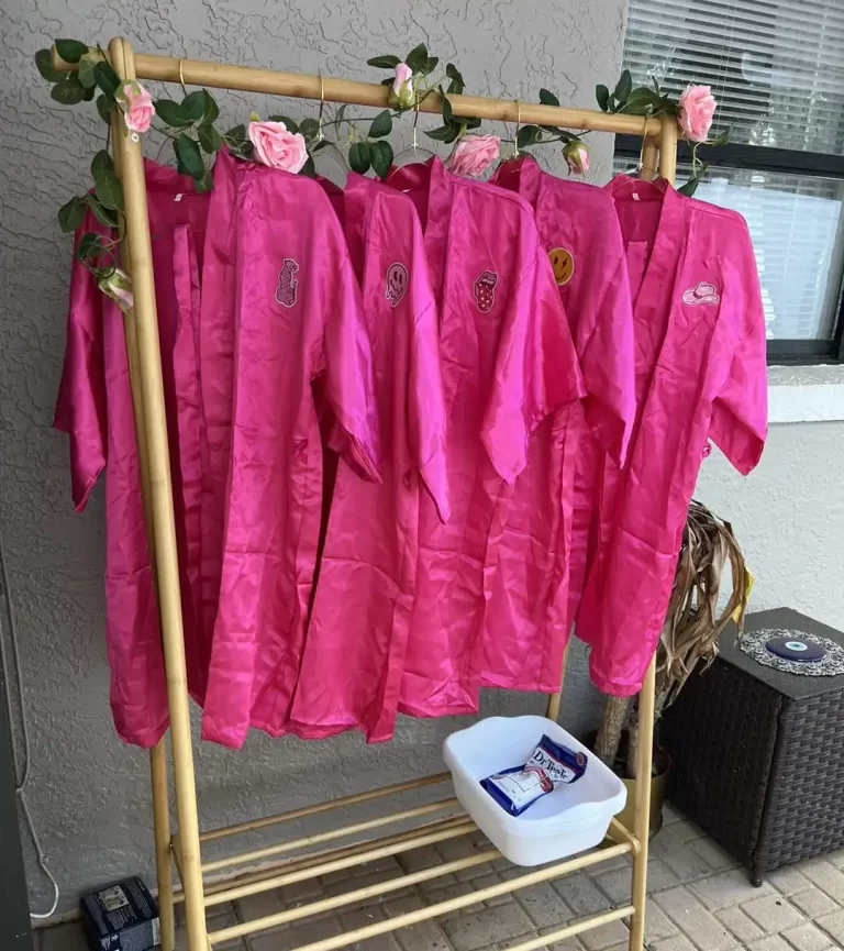 Pink choir robes hanging on a gold rack decorated with roses ready for a kids spa party with a white tub and a packet beneath it on a tiled patio set for a Spa Party with DIY lip Gloss.