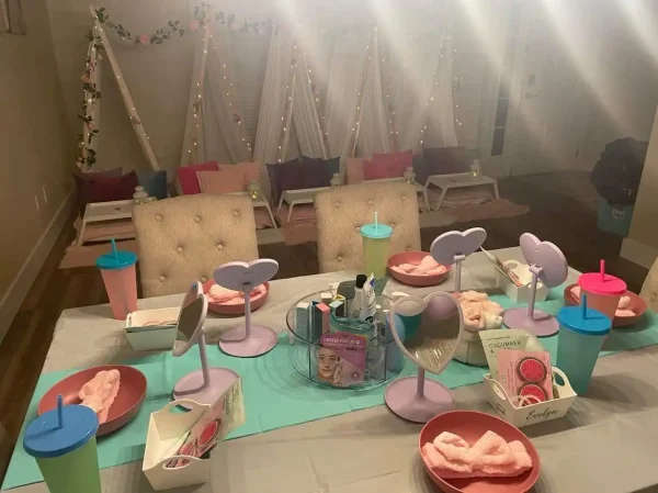 A Festival of Colors Party-themed party setup with chairs, face masks, towels, and bowls of pink facial cream on a decorated table.