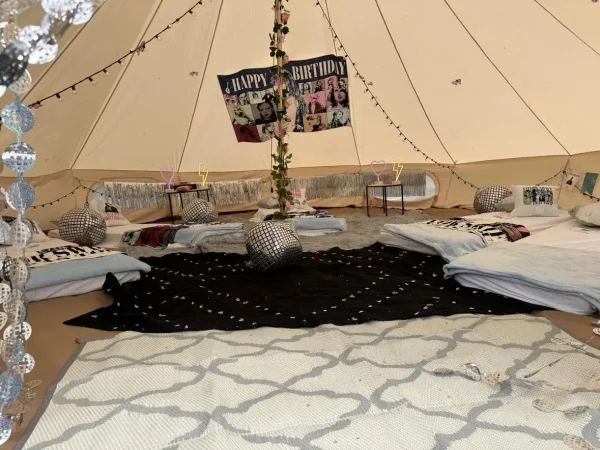 Interior of a tent decorated for a Dream Catcher Themed Party with multiple beds, a "happy birthday" banner, and Moroccan-style cushions.